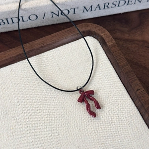 Close-up of a vintage red bow pendant necklace on a black cord over a textured backdrop