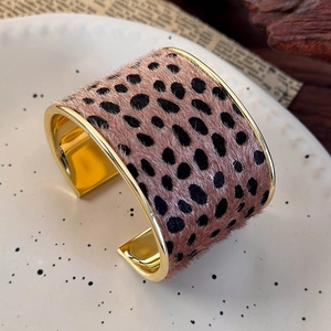 Close-up of golden wide open cuff bracelet with faux leopard fur texture on a white plate