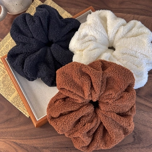 Close-up of three plush faux fur oversized scrunchies in black, cream, and brown colors