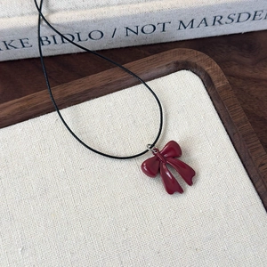 Close-up of a deep red bow pendant on a black cord necklace placed on a wooden tray