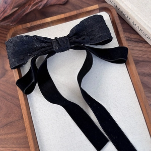 Detail of elegant black bow hair clip with textured jacquard and long velvet ribbons