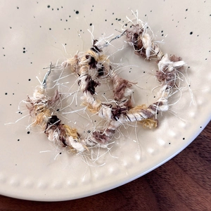 Dettaglio di orecchini a cerchio bohémien con trame di filato intrecciato marrone e beige
