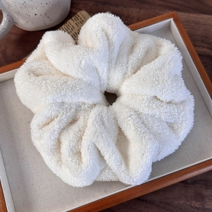 Macro shot of soft white plush scrunchie with rich pleated texture on wood background