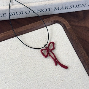 Macro detail of dark red enamel bow pendant on a black cord necklace for women