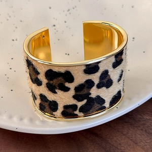 Detailed close-up of a wide gold cuff bracelet featuring leopard print suede inlay