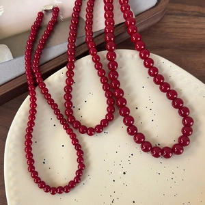 Détail du collier de perles en verre rouge foncé avec fermoir vintage sur plat céramique