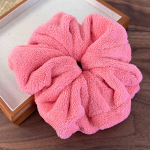 Detail of soft pink plush scrunchie showing thick fleece texture on a wooden background