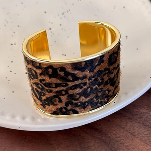 Close-up of leopard print faux fur texture and golden metal frame on a wide open cuff bracelet