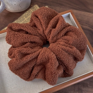 Detailed macro view of a large brown teddy fleece scrunchie on a wooden tray with soft texture