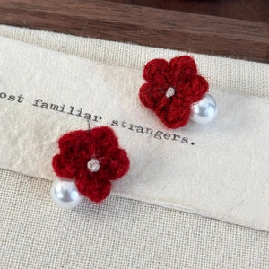 Macro detail of handmade dark red knitted flower earrings with a white pearl accent