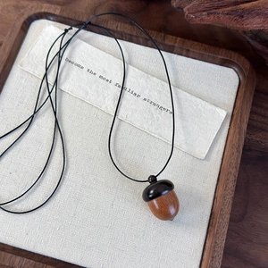 Macro detail of the vintage acorn wooden pendant with dual-tone texture and black cord