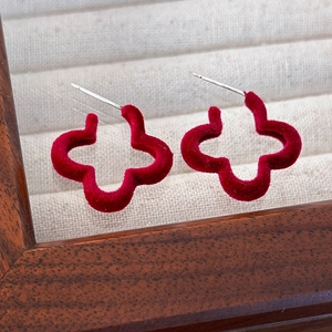 Détail de boucles d'oreilles trèfle floquées rouges sur un plateau en bois beige