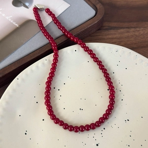 Détail des perles en verre rouge foncé et du fermoir en métal argenté sur un plateau