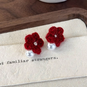Detail of red knit flower earrings with pearls on a vintage paper background