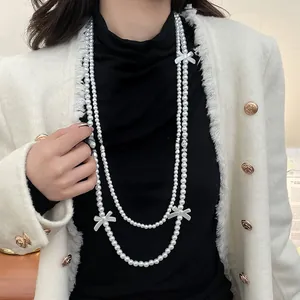 Detail of double-layer long pearl necklace with white bow accents on elegant model outfit