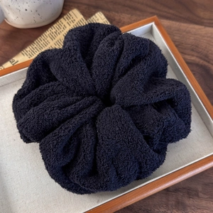 Macro detail of soft black towel-fabric scrunchie on a wooden tray with a vintage theme