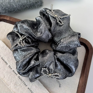 Detailed shot of silver-gray metallic scrunchie featuring elegant beaded bow accents