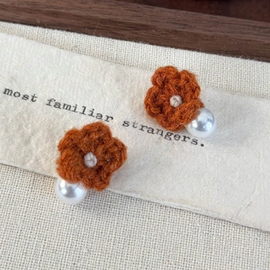 Macro detail of handmade knit flower earrings with pearls and orange crochet petals