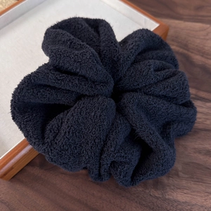 Detail shot of a large black scrunchie in soft towel fabric on a wooden tray