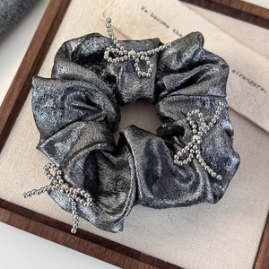 Close-up of a metallic silver scrunchie with three beaded bow accents on a display board