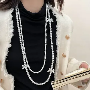 Detail showing double-layered pearl necklace with three elegant white bow charms on a model
