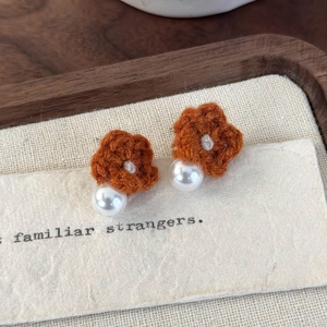 Detail of hand-knitted caramel flower earrings with white pearls for autumn and winter
