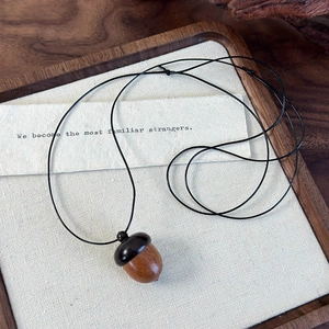 Handcrafted sandalwood acorn pendant necklace with black cord on a rustic wooden tray