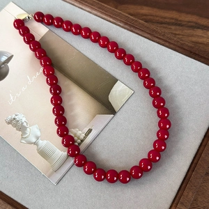 Détail des perles en verre rouge vif et du fermoir doré élégant sur ce collier rétro