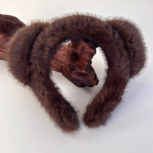 Gros plan sur la texture du bandeau en peluche marron posé sur un support en bois