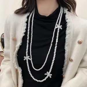 Elegant multi-layer long pearl necklace with white bow accents on black sweater