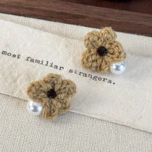 Close-up of brown knitted flower earrings with white pearls on artistic paper background