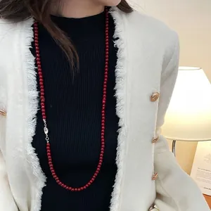 Détail d'un long collier de perles rouges porté sur une veste en tweed blanc élégante