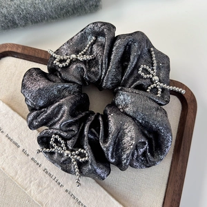 Close-up of silver beaded bow on shiny metallic scrunchie with satin texture details