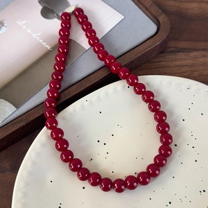 Détail d'un collier de perles rouge foncé avec perles en verre et fermoir blanc sur plateau