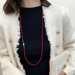 Détail d'un long collier de perles rouges avec fermoir argenté porté par un mannequin