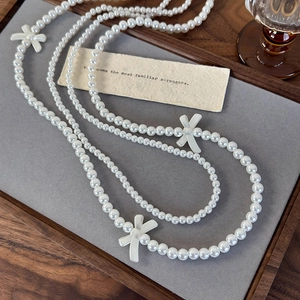Detailed view of long double-layered pearl necklace with white vintage bow accents