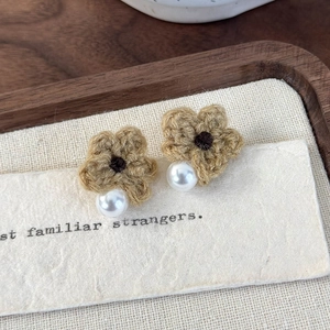 Detailed macro view of handmade khaki knit flower earrings with white pearl accents