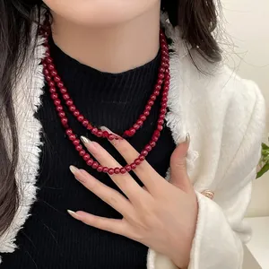 Gros plan d'un collier de perles rouge foncé à double rang sur une tenue chic
