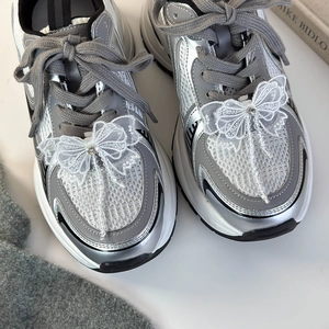 Détail d'un nœud en dentelle blanche et strass brillants sur des baskets compensées argent
