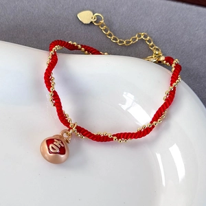 Macro detail of red woven bracelet featuring a gold lucky bag charm with Ji character