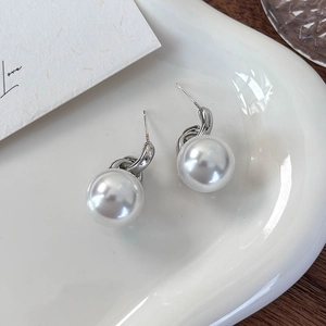 Detailaufnahme der eleganten weißen Perlenohrringe mit silbernen Haken auf Keramiktablett