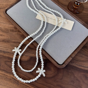 Detail of elegant double-layer long pearl necklace featuring white decorative ribbon bows