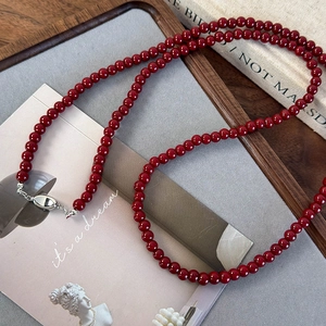 Détail d'un long collier de perles rouge foncé avec boucle argentée sur un livre