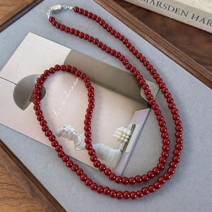 Long collier de perles bordeaux minimaliste avec fermoir argenté sur plateau gris