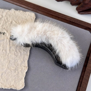 Close-up of white plush banana hair clip on a wooden tray showing soft faux fur texture