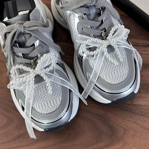 Dettaglio di fiocco in pizzo bianco con perle su sneaker in mesh argentato