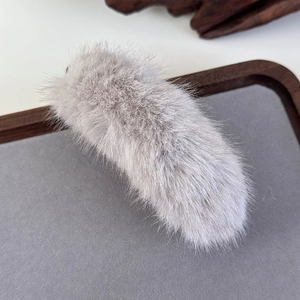 Close-up of soft light grey faux fur banana hair clip on dark wooden display tray