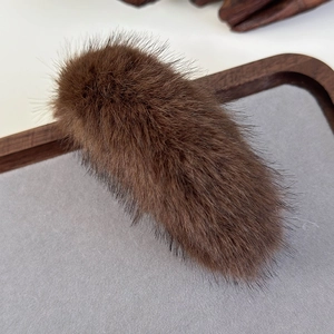Detailed view of coffee brown plush banana hair clip on a gray felt and wooden tray