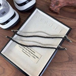 Detail of layered black beaded strand and silver metal chain accessory for footwear