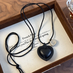 Detalle del colgante de corazón negro con placa grabada en collar de cuerda trenzada